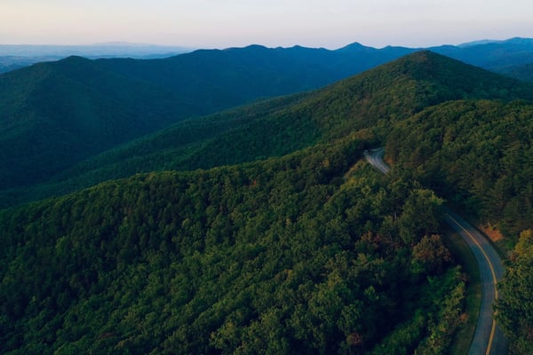 Aerial view of a winding Blue Ridge road through dense green forest at dusk