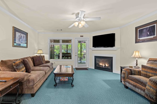 Living room with brown sofas, fireplace, TV, ceiling fan, glass doors to deck, and turquoise carpet